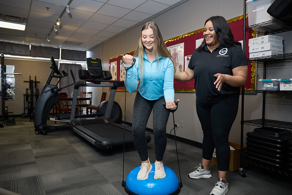 Students practice in lab. A woman stands on a balance while a student observes.