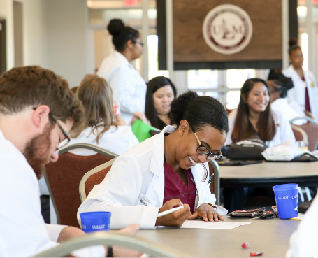 students in lab coats writing and smiling