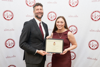 Dr. Joshua Stockley and Hattie Morgan smile at the camera. They hold an award.