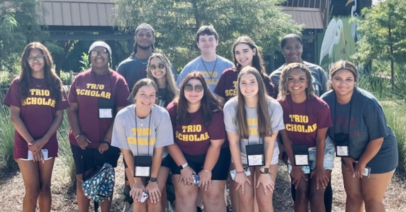 A group of students pose for a picture. They are wearing matching t-shirts that read "TRIO SCHOLAR".