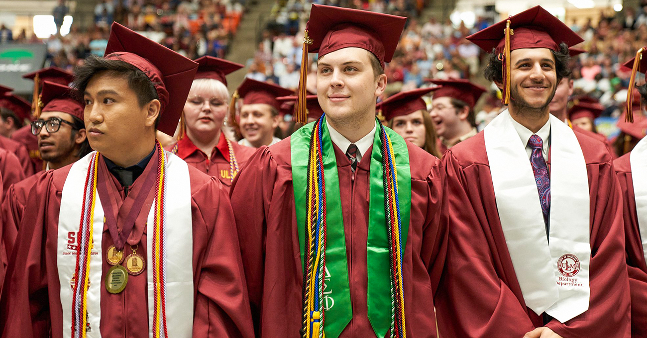 ULM graduates in caps and gowns smile and look off in the distance.